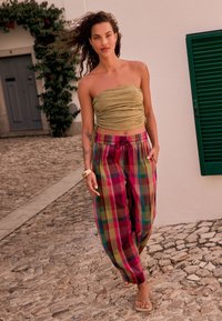 Olivovo zelený top bez ramienok s nariasenou textúrou v kombinácii s voľnými, pestrofarebnými károvanými nohavicami v odtieňoch ružovej, zelenej a žltej.