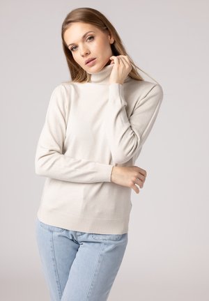 Light beige turtleneck sweater in soft knit fabric, featuring ribbed cuffs and hem, paired with light blue jeans, fitted silhouette.