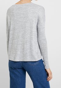 Haut gris en maille à manches longues avec une coupe décontractée, un col arrondi et un motif texturé, assorti à un jean en denim bleu.