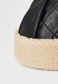 Chapeau en cuir noir matelassé avec une bande douce en fausse fourrure crème. Il présente une forme arrondie et des détails texturés sur le cuir.