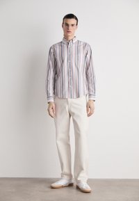Camisa de botones a rayas en colores pastel, con cuello estándar y mangas largas, combinada con pantalones rectos de color claro y zapatillas blancas.