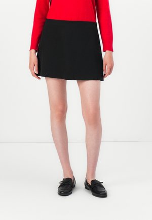 Svart skort med en jevn tekstur, tilpasset livlinje og A-linjeform. Kombinert med svarte loafers og en langermet rød topp.