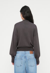 Σκούρο γκρι πλεκτό πουλόβερ με φουσκωτά μανίκια, ριμπ λαιμόκοψη και τελείωμα, συνδυασμένο με ανοιχτό μπλε τζιν ψηλόμεσο με πίσω τσέπη.