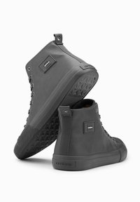 Zapatillas altas en goma y cuero gris, con una suela texturizada, acentos de metal y cordones planos. Presenta una placa de logo en el costado.