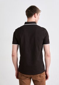 Brown polo shirt with a short collar, white trim along the collar and sleeves. Worn with light brown pants, showcasing a plain back view.