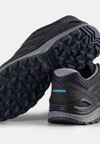 Black trail running shoes with textured mesh upper, reinforced heel, and aggressive rubber outsole. Features turquoise logo on heel.