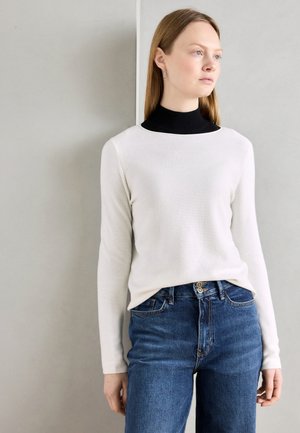 Maglione bianco a maniche lunghe con un sottogiacca nero a collo alto, abbinato a jeans in denim blu. Texture liscia, design minimalista, stile semplice.
