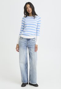 Pull rayé bleu et blanc à manches longues, associé à un jean bleu délavé à jambes larges et des chaussures noires. Coupe simple et texture douce.