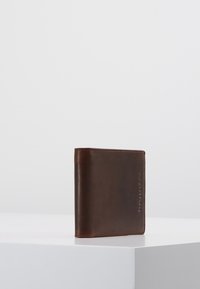 Brown leather wallet with a smooth texture, bi-fold design, and embossed accents on the side. Minimalist and compact shape.