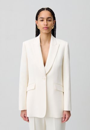 Blazer bianco su misura con design aderente, rever a punta, chiusura con un bottone e tasche frontali. Tessuto liscio con silhouette strutturata.