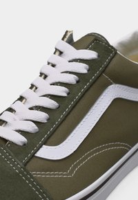 Κοντινό πλάνο αθλητικού παπουτσιού σε ελιά πράσινο με λευκή πλαϊνή ρίγα, λευκά κορδόνια και λευκή ραφή σε μουσαμά και σουέντ υλικά.