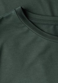 Ciemnozielony materiał t-shirtu z bawełny, z okrągłym dekoltem i gładką teksturą, z płaskim szwem i bez dodatkowych wzorów ani akcentów.