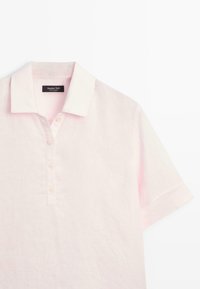 Lichtroze polo met korte mouwen, kraag en vier knopen aan de voorkant, plat liggend op een witte achtergrond.