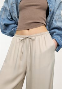 Ljust beige byxor med avslappnad passform, elastisk midja och dragsko. Matchas med en ribbade brun topp och en blå denimjacka.