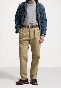 Chaqueta vaquera sobre un jersey de cuello alto gris, pantalones khaki con pliegues y zapatos marrones con diseño de cordones. Incluye un cinturón marrón y tejidos con textura.