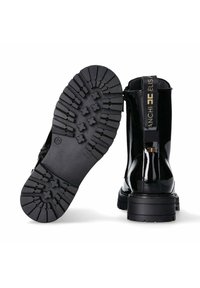 Stivali alla caviglia in pelle verniciata nera con suola in gomma con battistrada spesso. Presentano una cerniera e un'etichetta con logo sul retro per una vestibilità sicura.