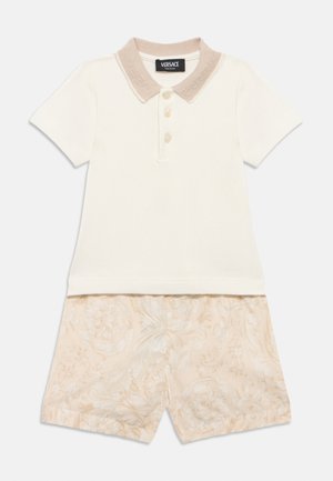 Kortærmet cremefarvet polo med beige krave og beige shorts med blomsterprint, stylet som et koordineret sommeroutfit.