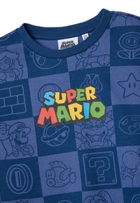 Camiseta de algodón azul marino con un gráfico multicolor de "Super Mario", con ilustraciones de personajes contorneados en un patrón de cuadrícula.