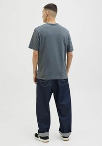 Grå kortærmet t-shirt med en afslappet pasform, parret med løse mørkeblå jeans med opfoldede ærmer. Simpelt design uden mønstre eller accenter.
