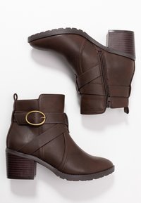 Botas de tobillo de poliéster marrón con cremallera lateral, detalle de tira cruzada, acento de hebilla dorada y tacón apilado. Suela de goma texturizada.