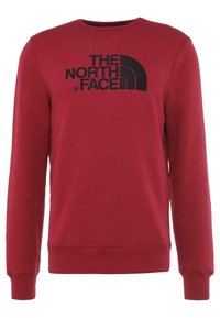 Sudadera roja de manga larga, con puños y dobladillo acanalados, que presenta un gran logo negro en la parte frontal. Fabricada con un tejido suave y texturizado.