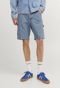 Denim shorts in light blue, featuring a relaxed fit and frayed hem. Worn with white socks and blue sneakers with white stripes.