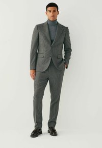 Gray checkered suit with fitted trousers, single-button jacket, and high-neck gray top. Smooth texture, tailored design, and dark shoes.