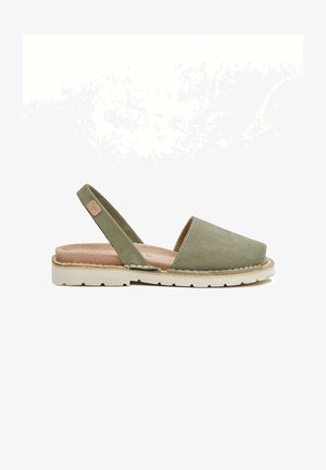 Sandal de ante verde con tacón abierto, suela plana y puntera descubierta, y una plantilla beige. Presenta un borde cosido y una etiqueta de logo en color marrón en el talón.