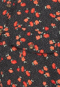 Tecido preto com pequenas bolinhas brancas e um padrão floral com rosas vermelhas. Dois botões castanhos na área do bolso.