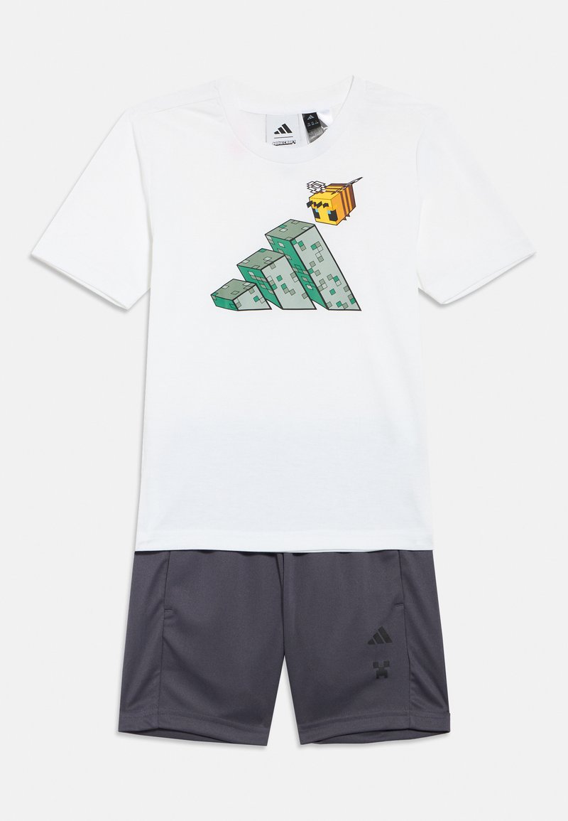 Biela košeľa s krátkym rukávom s pixlovaným motívom včely a kamenného bloku, doplnená sivými krátkymi nohavicami s malými logami na ľavej nohe.