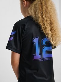 Child with curly hair wearing black sports jersey numbered 12 with "Light Up The World" text on the back.