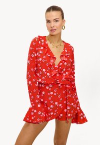 Vestido floral rojo con detalles de volantes y mangas largas. Hecho de una tela ligera con patrones de flores rosas y un cinturón de lazo.