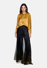 Yellow snake-patterned silk blouse paired with sheer black wide-leg pants, featuring elegant pleats and a chain accent at the waist.