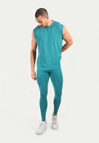 Miętowy top bez rękawów w połączeniu z dopasowanymi legginsami, oba wykonane z elastycznego materiału. Białe trampki dodają kontrastu do stroju.
