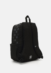 Sac à dos noir avec des bretelles rembourrées, comprenant une poche avant et un compartiment en maille sur le côté. Décoré de motifs de logo subtils et d'un emblème blanc.