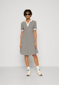 Gestreiftes Polokleid in Schwarz und Weiß, mit V-Ausschnitt, kurzen Ärmeln und ausgestellter Silhouette. Trage es mit weißen Sneakers und Socken.