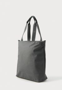 Γκρι τσάντα χεριού φτιαγμένη από ανθεκτικό ύφασμα. Διαθέτει κοντούς χειρολαβούς με ανάγλυφα λογότυπα. Ορθογώνιο σχήμα με ραμμένες άκρες.