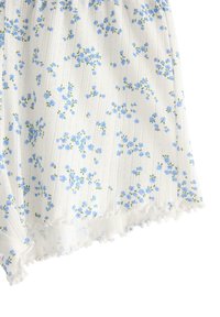 Hvidt stof med blåt blomsterdesign og grønne accenter, der har en ribbet tekstur og en flæset kantdetalje nederst.