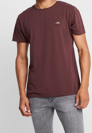 Bordowa bawełniana koszulka z krótkim rękawem, okrągłym dekoltem i małym logo na piersi. Połączona z szarymi dżinsami.