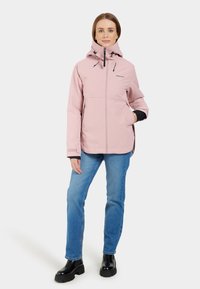 Ljusrosa vattentät jacka med huva, framdragkedja, justerbara snoddar och svarta detaljer, ihop med blå jeans och svarta stövlar.