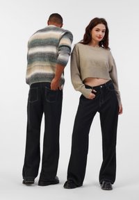 Pull en tricot avec des rayures vertes, beiges et grises ; pull beige court ; jean noir à jambes larges ; chaussures robustes noires ; accessoires minimalistes.