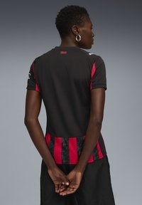 Maillot de sport à manches courtes noir et rouge avec un bas en motif noir texturé et le texte « MILAN » au dos près du cou.