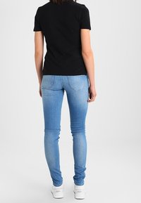 Camiseta negra de mangas cortas combinada con unos vaqueros skinny azul claro. El conjunto incluye zapatillas blancas, con una textura de tela suave.