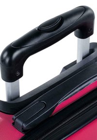 Asa de maleta rodante con un agarre negro texturizado y marco de metal, unida a un cuerpo de tela de color rosa brillante con detalle de cremallera.