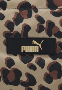 Tissu imprimé léopard avec des taches noires et marron, comportant un patch rectangulaire noir avec le logo Puma doré et du texte.