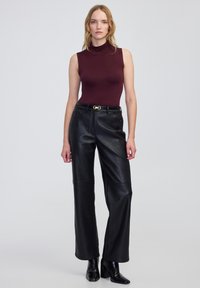 Bordeaux mouwloze coltrui gecombineerd met hoge zwarte leren broeken en zwarte hakken enkelboots. Gouden gesp riem als accent.