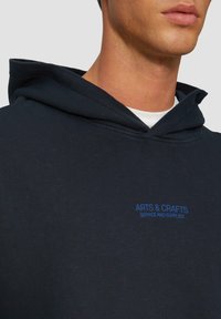 Marineblauwe hoodie gemaakt van een katoenmengsel met een voorzak en een capuchon met trekkoord. "ARTS & CRAFTS" logo in blauwe borduring.