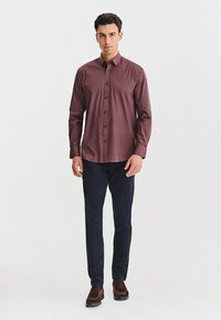 Burgundowa koszula z długim rękawem w wzór, zestawiona z ciemnoniebieskimi spodniami. Koszula ma delikatny geometryczny wzór i klasyczny kołnierzyk.