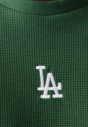 Tela verde de punto waffle con las letras superpuestas "LA" bordadas en blanco cerca del centro.