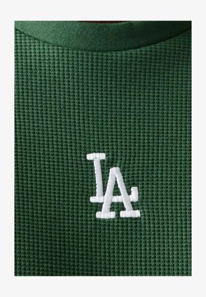 Tela verde de punto waffle con las letras superpuestas "LA" bordadas en blanco cerca del centro.